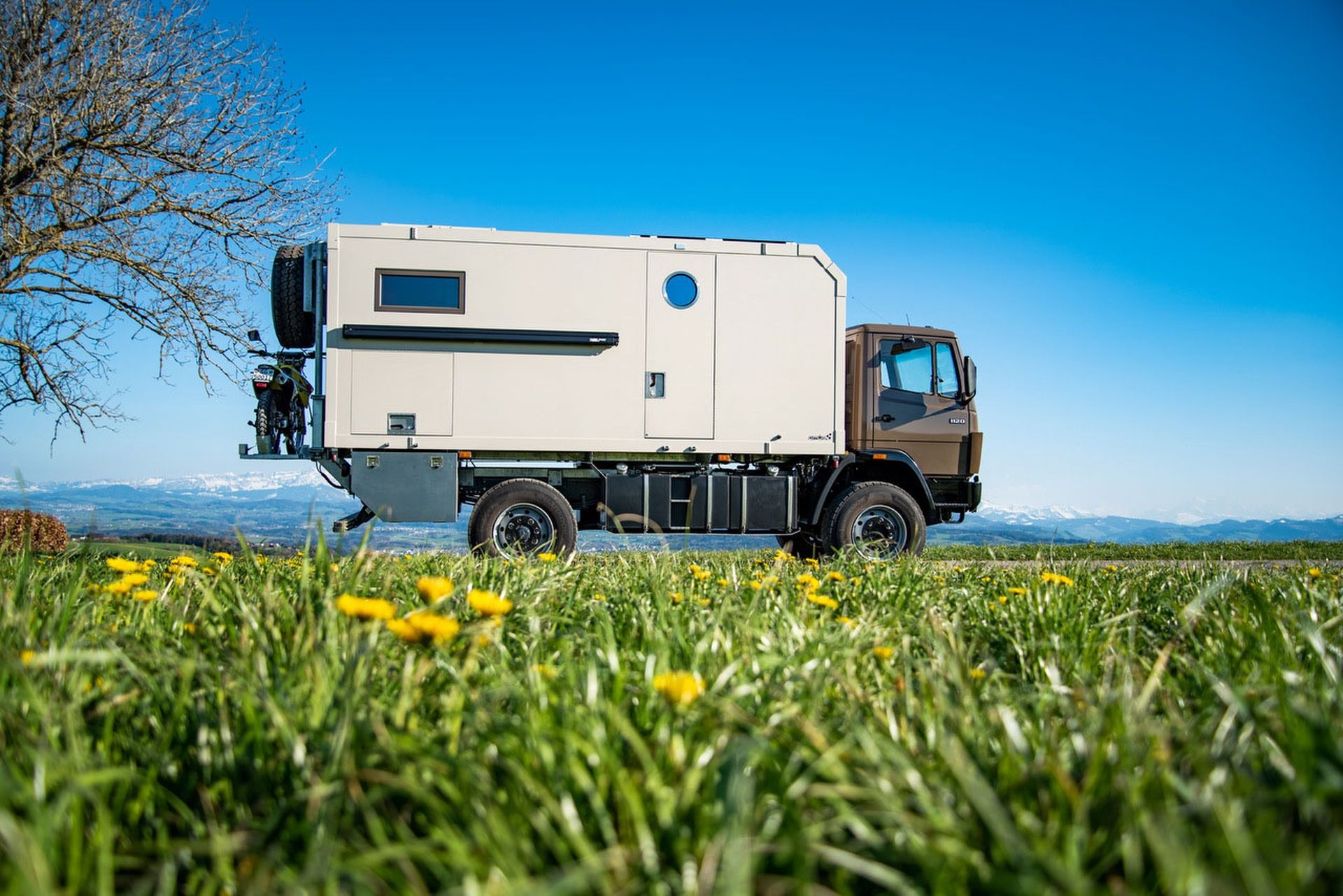 Mercedes Unimog mit einem Kistenaufbau und einem Motorrad hinten aufgebockt