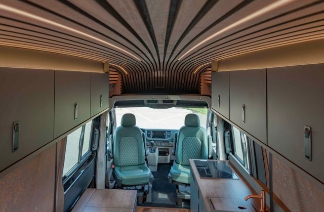 Innenausbau von Cocoon Vans eines VW Crafters 4x4 mit Holzakzenten aus amerikanischem Nussbraum, zwei grünen Ledersitzen, viel Stauraum über Kopf und einem kompakten Küchenbereich.