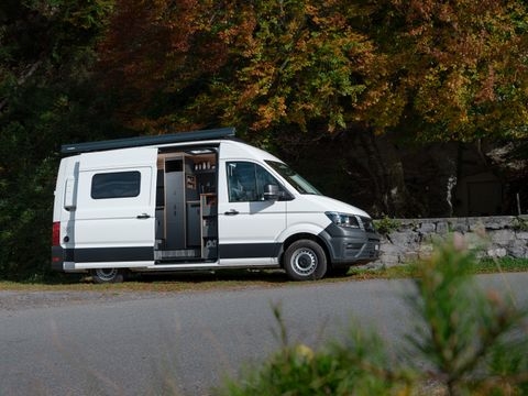 Kleinserie Patgific von Cocoon Vans in der aussenansicht. Ein wiesser VW Crafter mit geöffneter Schiebetür die den Blick auf einen Teil der Küchen freigibt